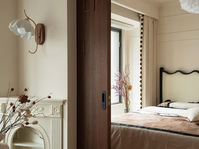 A calm bedroom with a wooden door, a large bed, two vases, and a potted plant, with natural light from the window
