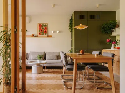 Open plan living and dining area with a wooden dining table, potted plant, and comfortable couch, surrounded by chairs and vases