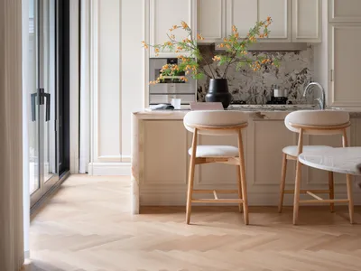 Modern kitchen with white cabinets, wooden floors, and a center island with stools, featuring a potted plant and three cups on the counter