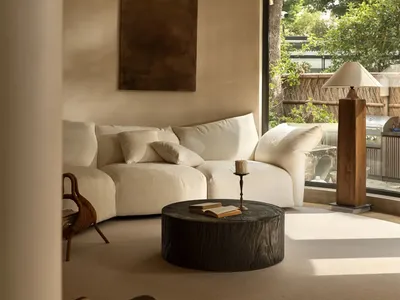 Bright and inviting living area with a white couch, two chairs, a dining table, and a book on the couch, surrounded by sunlight streaming through the window