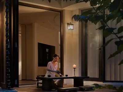 A well-lit living area with a woman sitting at a table, surrounded by a couch, chair, and TV, creating a cozy atmosphere