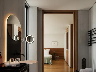 Well-lit bedroom with wooden floors and walls, featuring a large mirror, two beds, and a chair, creating a cozy and inviting atmosphere