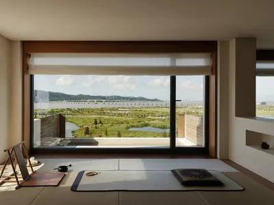 Cozy living space with a wooden floor, two couches, a chair, and a dining table, with a large window offering a scenic view of the surrounding landscape