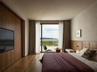 A serene bedroom with two beds, a chair, and a dining table, offering a view of the ocean through a large window