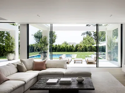 An inviting open living area with a white couch, chairs, a dining table, and decorative items, lit by natural sunlight through glass doors