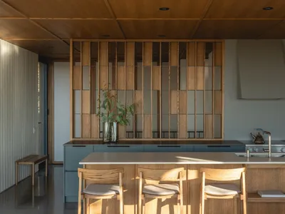 A modern kitchen with wooden cabinets and a wooden countertop, featuring a sink, refrigerator, and potted plant, in a well-lit space with a warm atmosphere