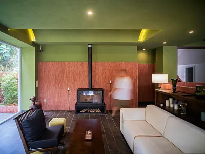 Cozy living room with a fireplace, green walls, and a dining table, surrounded by a couch and a chair