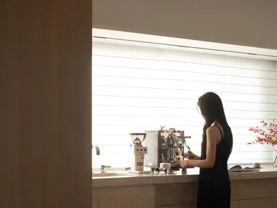 一名女性站在家中廚房,在一個有家的、放鬆的氛圍中準備飲料,身邊有水槽、冰箱和植物罐