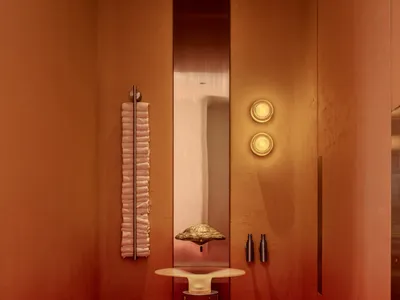 Bathroom with a red accent wall, a white sink on a red table, and two bottles, set in a well-lit space with a warm atmosphere