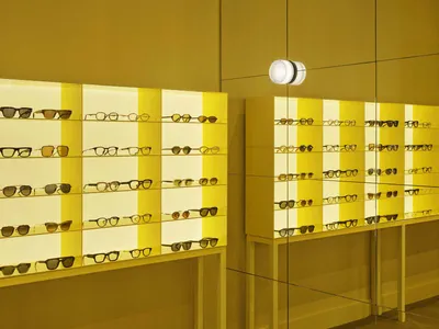 一副彩色眼鏡展示架，展示著不同款式和顏色的眼鏡，對著一面黃色背景，使用設計好的照明創造了一個溫馨的氛圍