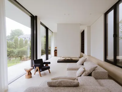 A well-lit living room with a white color scheme, featuring a couch, chair, and fireplace, with a large window providing natural light