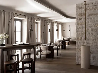 A well-lit restaurant interior with a long wooden table and multiple chairs, surrounded by additional seating and wooden furnishings