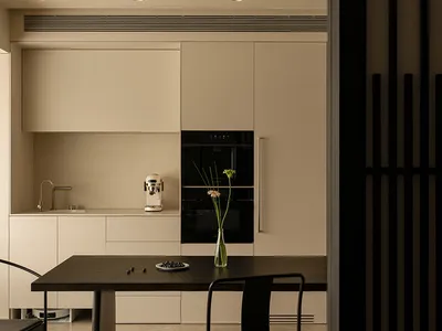 A modern kitchen with a wooden table, glass accents, and a dimly lit atmosphere, featuring a dining area with chairs, a microwave, and a vase with a flower
