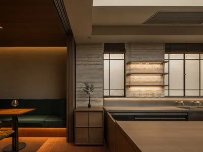Modern kitchen with a wooden countertop, dining table, and potted plant, featuring a sink, refrigerator, and wine glass, with soft and warm lighting