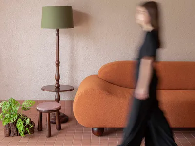 A woman walks towards a couch in a warm and inviting living room with brown furniture and natural lighting