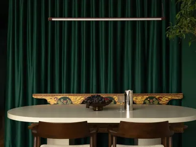 Dining room with a white table and chairs, surrounded by green curtains, and a bowl of fruit on the table, with soft and inviting lighting