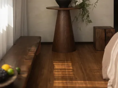 一間舒適的客廳隔間，地板是木地板，床、躺椅、玻璃花瓶裝著白色的花，放在桌子上，透過窗戶進入的自然光線