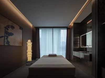 A dimly lit bedroom with a white bed, a wooden bed frame, and a brown window frame, set against a neutral background