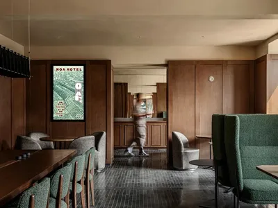 A hotel lobby with a dining table surrounded by chairs, a wooden floor, and a large mirror on the wall, set in a well-lit space with a welcoming atmosphere