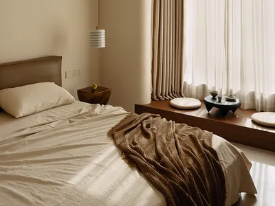 A well-lit bedroom with a bed, window, and table lamp, featuring wood and fabric materials in a warm and inviting space
