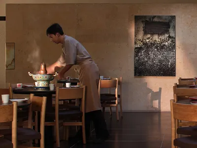 A modern restaurant dining area with wooden tables and chairs, well-lit by natural light and warm ambiance