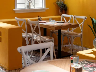 A modern dining area with a yellow wall, a table set with plates, cups, and a bottle, surrounded by chairs and a potted plant, creating a cozy and inviting atmosphere