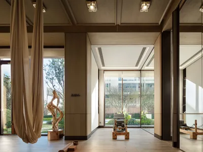 A well-lit living area with a wooden floor, a chair, and a bench, featuring a large window for natural light and a warm, inviting atmosphere