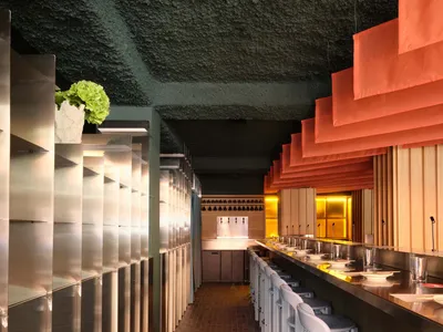 A dimly lit restaurant interior with a long dining table, chairs, and potted plants, set in a modern and inviting space