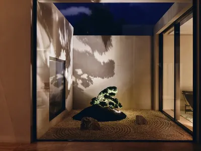 A cozy living room with a small potted bonsai tree surrounded by rocks, a couch, and a chair, creating a warm and inviting atmosphere