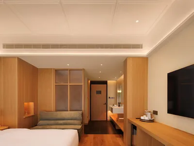 Cozy bedroom with a bed, couch, and mirror, surrounded by wooden furniture and a wooden floor, in a well-lit space