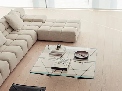A living room with a large couch, glass coffee table, and bookshelf, featuring a clean and modern appearance with a wooden floor and predominantly white furniture