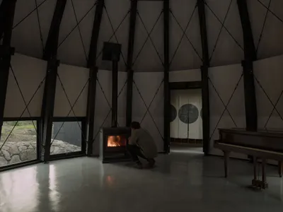 A man sits in front of a fireplace in a cozy living room with a piano in the corner