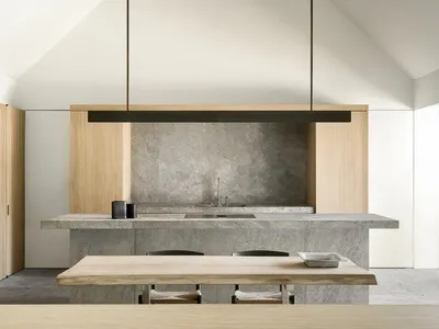 A modern kitchen with a wooden table and marble top, surrounded by black chairs, a sink, and a hanging light, with natural lighting creating a warm atmosphere