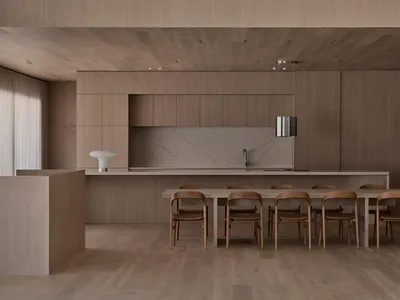 Modern kitchen with wooden floors and cabinets, featuring a sink, refrigerator, dining table, and chairs, with a vase on the table, under soft and warm lighting
