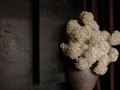 一間溫馨的生活空間，牆面為黑色，桌面為棕色，桌上有一個白色花瓶裝著白色花