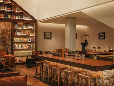 Cozy living space with a wooden floor, a wooden bar, and wooden stools, surrounded by books and a comfortable seating arrangement