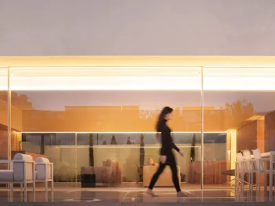 A woman walks through a well-lit room with a glass wall and glass floor, featuring a couch and dining table in a comfortable and inviting atmosphere