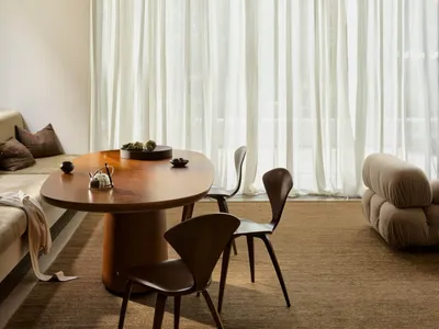 Cozy modern living room with a dining table, chairs, couch, and wooden furniture, featuring a mix of natural and artificial lighting