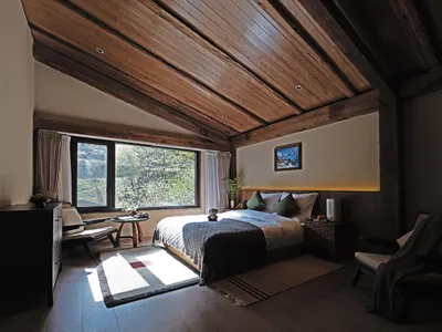 Cozy bedroom with a bed, chair, and window, featuring a wooden floor and ceiling, and well-lit with a bright atmosphere