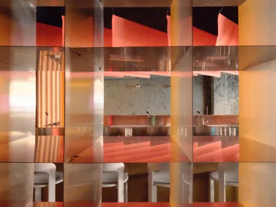 A modern restaurant interior with a wooden dining table surrounded by white chairs, a red accent wall, and dim lighting creating a cozy atmosphere