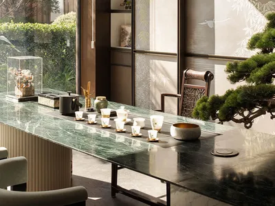 A well-lit living room with a glass table, a chair, and warm decorations, set against a backdrop of a large window and natural light