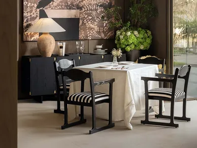 Dining room with a table set for a meal, surrounded by chairs, wine glasses, and vases, with a large painting on the wall in a well-lit, modern space