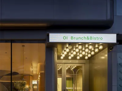 A modern restaurant entrance with a glass door, lighted sign, and warm lighting, featuring chairs and dining tables inside