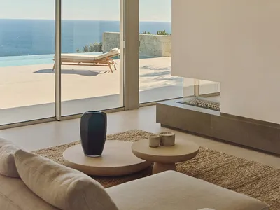 Coastal living room with a couch, chair, dining table, and fireplace, filled with natural light from a large window overlooking the ocean