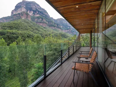 Cozy living room with a wooden floor, a couch, chairs, and a large glass wall offering a view of the mountains