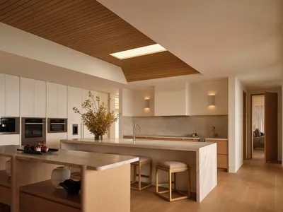 A modern kitchen with a wooden floor and white cabinets, featuring a sink, refrigerator, and microwave, with dim lighting creating a cozy atmosphere