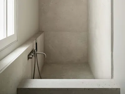 A clean bathroom with a white concrete shower stall and a window, well-maintained and minimalist