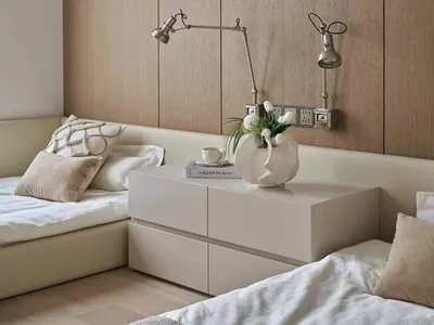 A well-lit bedroom with a bed, dresser, and lamp, featuring wood and white surfaces