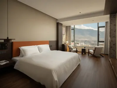 A well-lit bedroom with a wooden floor, a bed, a chair, and a table, near a window
