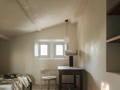 A well-lit bedroom with a bed, chair, and desk, featuring a white color scheme and wooden furniture